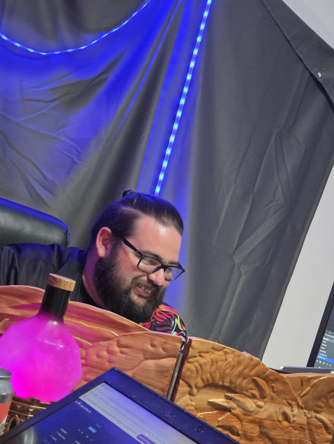 John smiling behind the GM screen with a pink potion bottle