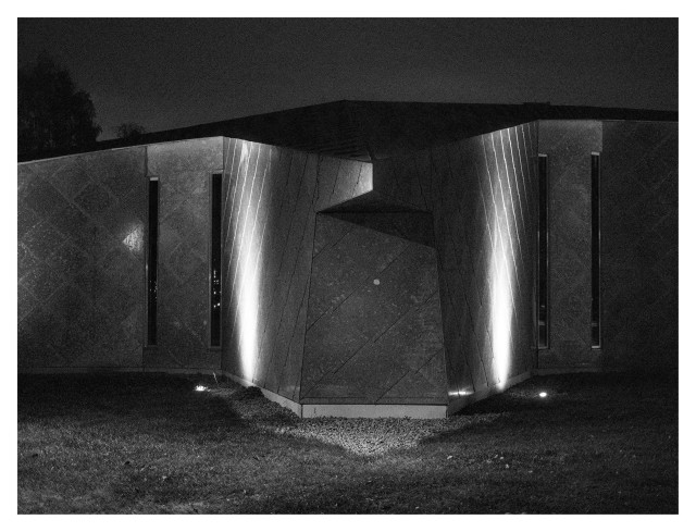 En liggande svartvit bild på en byggnad med 4 mycket smala, vertikala fönster. Formen på byggnaden är mycket modern och silverfärgad.