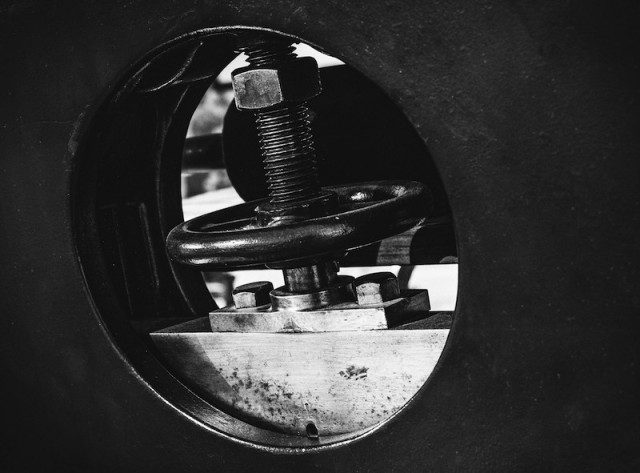 Das Bild zeigt die Nahaufnahme eines Flansches mit einem Handrad und einer großen Schraubenverbindung, die typischerweise in industriellen Rohrleitungssystemen wie Öl- und Gasanlagen verwendet werden. 