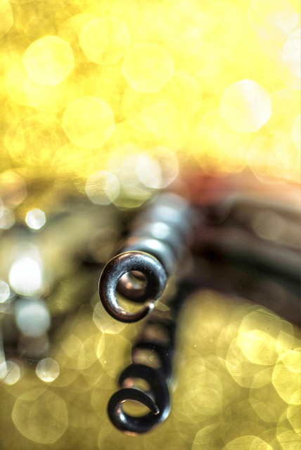 Auf dem Bild ist die Metallspirale eines Korkenziehers in Nahaufnahme zu sehen.
Die scharfe Darstellung konzentriert sich auf die gewendelte Spitze des Korkenziehers.
Der Hintergrund ist unscharf (Bokeh-Effekt) und besteht aus vielen hellen, gelben und weißen Lichtkreisen.