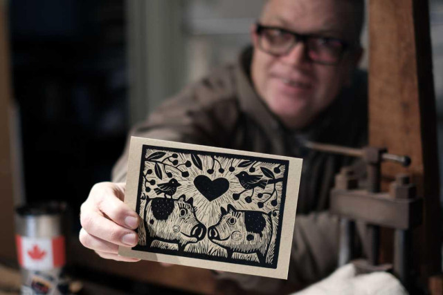 artist holding a linocut greeting card that depicts two adorable piggys touching snouts.  