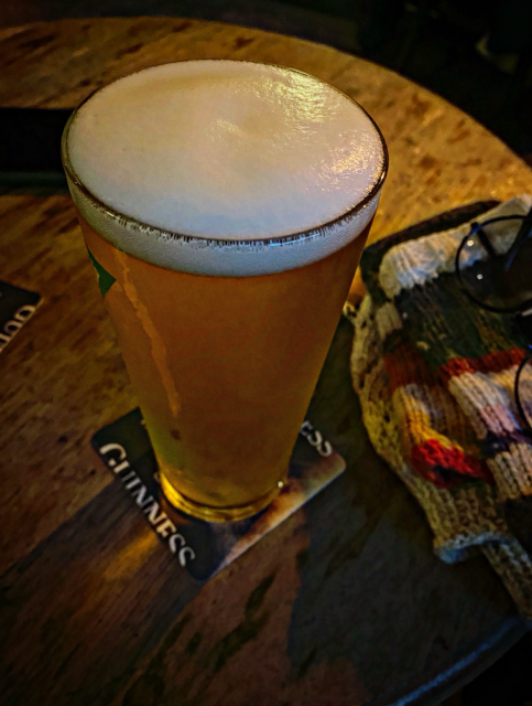 En pint med Tuborg sedd ovanifrån. Stickad mössa och handledsvärmare ligger bredvid med ett par runda glasögon ovanpå. Träbordet under är trevligt slitet. 