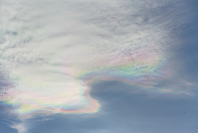 Thin clouds in a pale blue sky. The edges of the clouds shimmer in mother-of-pearl colors.