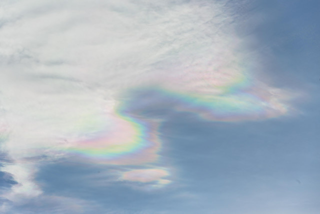 Thin clouds in a pale blue sky. The edges of the clouds shimmer in mother-of-pearl colors.