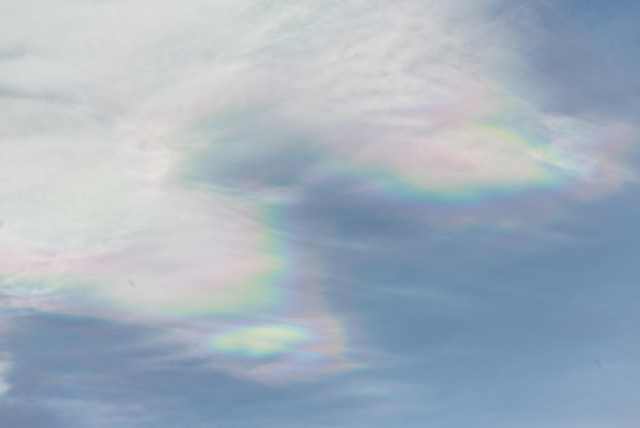 Thin clouds in a pale blue sky. The edges of the clouds shimmer in mother-of-pearl colors.