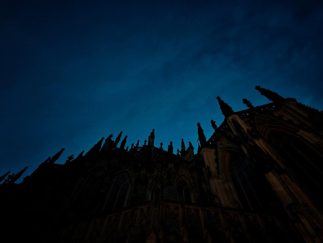 A wide-angle photo looking up along a dark silhouette of a gothic-style building with pointed spires leading into a deep blue sky.