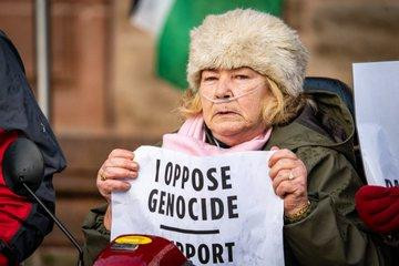 A lady sitting on a motability scooter holding a sign reading I OPPOSE GENOCIDE I SUPPORT PALESTINE ACTION