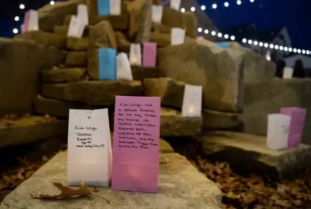 Pink, white and blue paper bags with messages written on and candles inside, placed on a shrine.