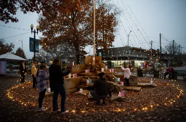 People gatehr around the stone monument, encircled by candles.