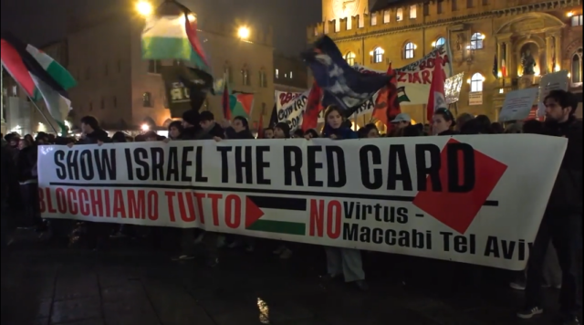 Large crowd with flags and placards march behind a banner reading SHOW ISRAEL THE RED CARD/BLOCCHIAMO TUTTO