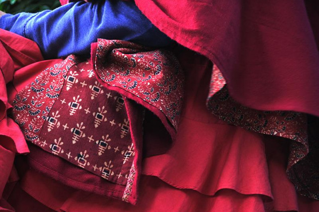 C'est une photo au format paysage, en plan rapproché d'un costume de scène dont la couleur dominante est le rouge.
Dans l'angle supérieur gauche, on voit la manche d'un vêtement bleu . Le reste de l'image est dans des tons de rouge apparents sur ce qui pourrait être le bas d'une cape, trois étages de volants et de deux pièces de tissus dont l'usage m'échappe. Certains, sur la gauche  portent une impression à motifs régulier.  Même vu partiellement ce costume est impressionnant.