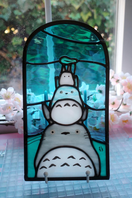 Backlit stained glass art featuring 3 Totoro stacked on top of each other.