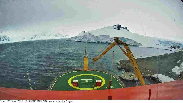 View from a webcam mounted on the RRS Sir David Attenborough boat. Typically you'd see the front of the ship with a helipad, and the sea waters surrounding the ship. Depending on the current location of the ship, the scenery may include icebergs and industrial ports.