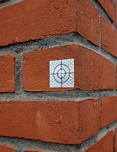 A photo showing a small reflective survey target sticker is placed on a red brick corner.