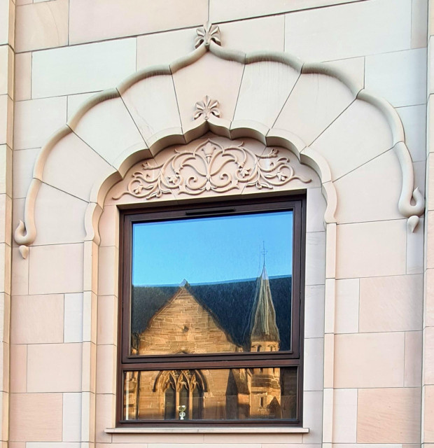 A section of a Victorian gothic church reflected on the window of a modern sikh temple.
