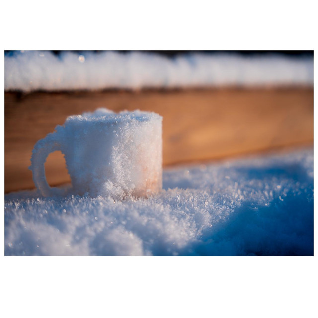 Eine Glühweintasse steht auf einem Tisch. Seit dem diese da abgestellt wurde, hat es geschneit. 