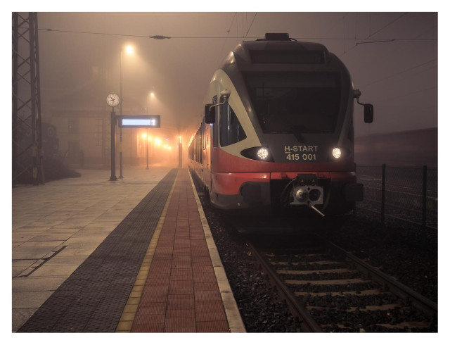 Eine S-Bahn steht still an einem nebligen Bahnsteig bei Nacht. Der Bahnsteig ist menschenleer, die Uhr und Anzeigetafel sind nur schemenhaft erkennbar.