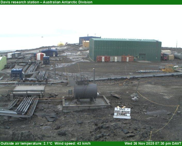 A view of the Davis research station with research buildings, equipment, and vehicles scattered around, and mountains visible in the background. Occasionally features Happy Birthday signs.