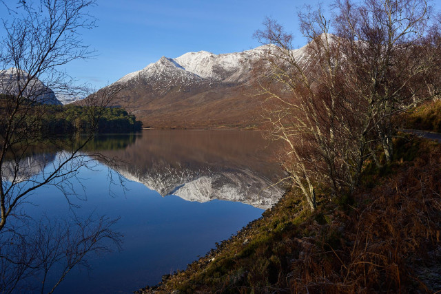 Framed by trees either side some of the snow capped peaks of Beinn Eighe reflected in Loch Clair.
