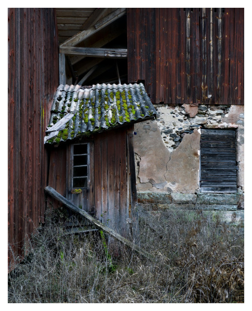 En stående bild på en röd ekonomibyggnad i trä och sten med två dörrar. Den ene i rött trä med ett smalt vertikalt fyrdelat fönster, den andre i svart trä.