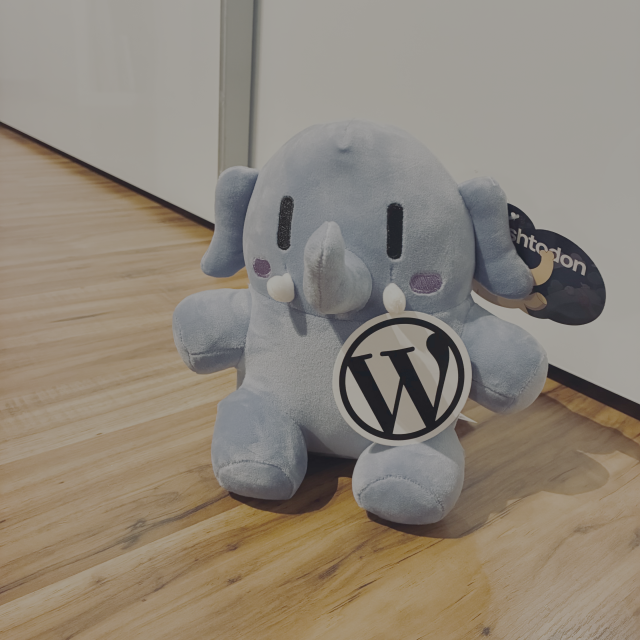 A Plush Mastodon holding a WordPress Sticker