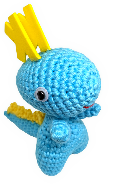 A cute, cheeky-looking aqua-blue amigurumi dragon called "Karmen" looks into the camera.