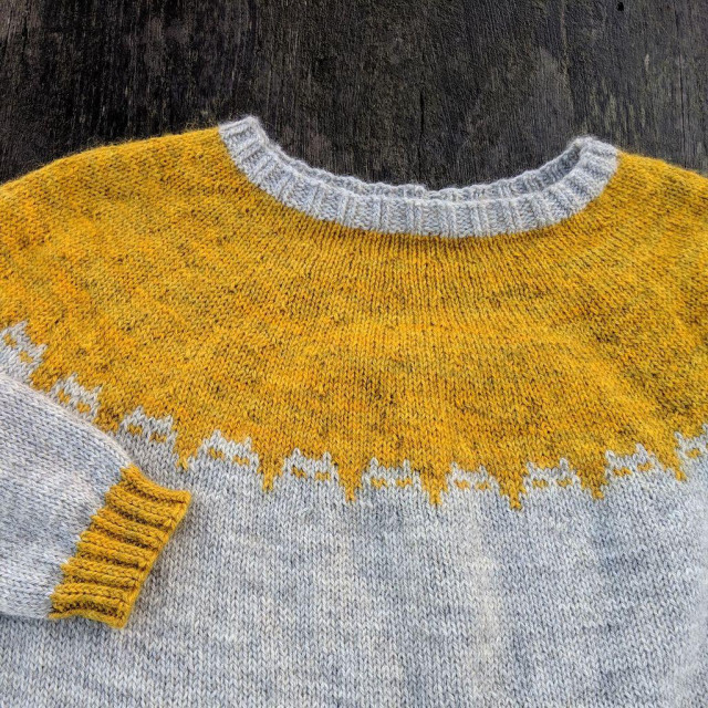 A close up of the yoke of a round-yoke sweater in gray and yellow. It has cats that are staring at you.