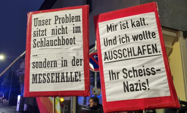 Foto 2er Schilder:
"Unser Problem sitzt nicht im Schlauchboot, sondern in der Messehalle."
"Mir ist kalt. Und ich wollte ausschlafen. Ihr Scheiss-Nazis!"