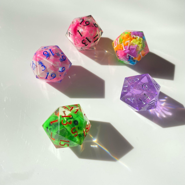 A d20 set in bright colors:
Pink orb with silver heart decals
Pink and white marbled with silver stars
Green and black skulls
Translucent lavender with microglitter
Neon color mini gummi bears