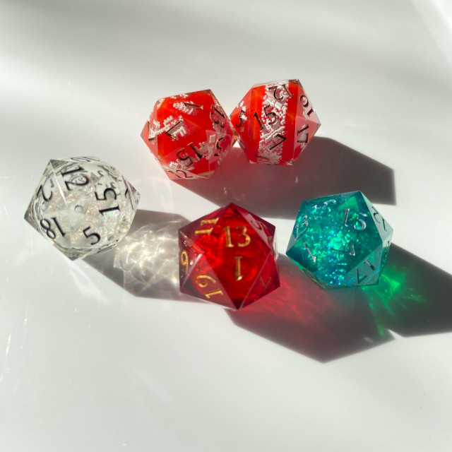 A d20 set in holiday colors:
Two red with white decals that look like sweaters
One clear with a liquid core of white glitter like a snowglobe
One ruby red with a gold glitter liquid core
One emerald green with crinkled mylar