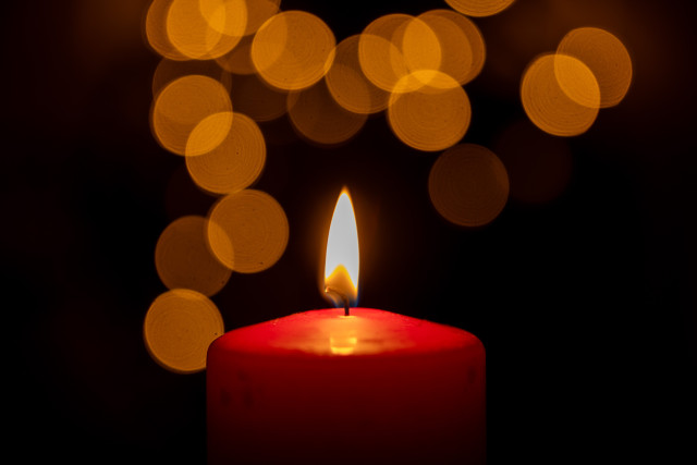 Eine rote Kerze brennt. Dahinter große runde Bokeh Lichter.  

A red candle is burning. Behind it are large round bokeh lights.  