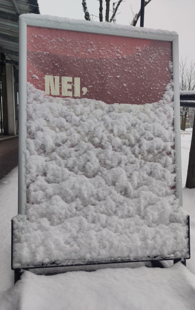 A stand-up advertising board snowed over so only the first word "NEI", Norwegian for "no", is visible in white letters on a red background. 