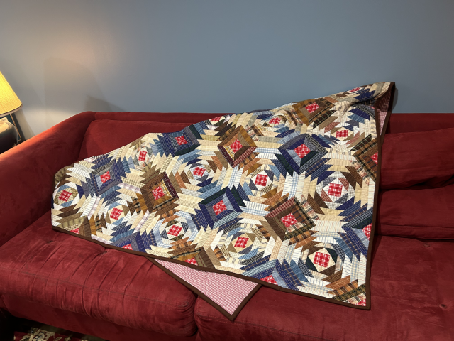 The quilt is lying on a red coach in a way that really makes a wheel and spoke aspect of it pop out. There's just a corner peaking out of the underside to show that the backing is a pink check.