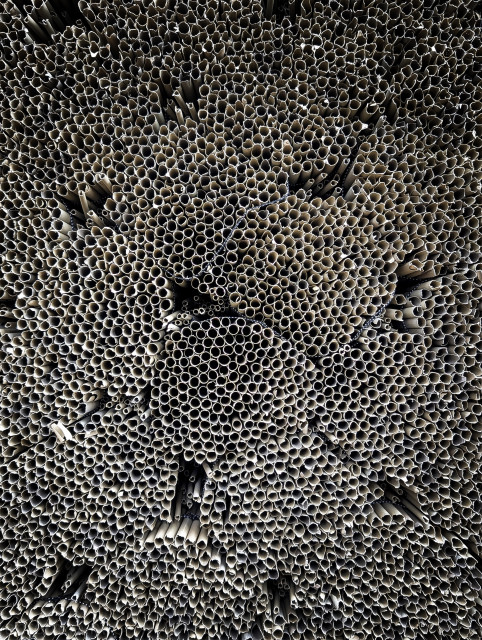 A huge pile of bundles of reed. The surface is dominated by the circular cross-sections of countless tubes packed tightly together. The repetitive texture resembles a honeycomb or the cells of an organism when viewed from a distance.

The color palette is monochromatic or near-monochromatic, featuring shades of grey, beige, and brown. If you look more closely, you can see the metal wire used to make the bundles as black and white, dotted lines.