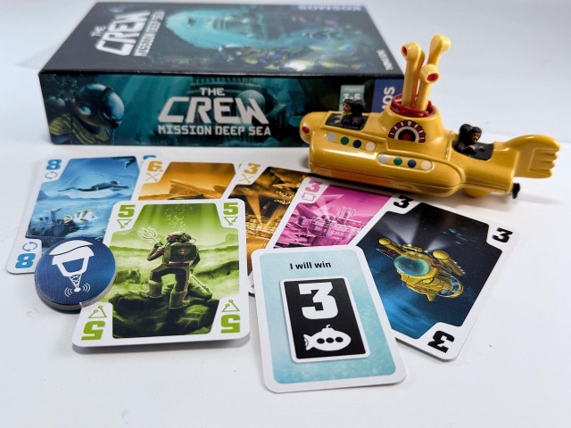 The Crew Mission Deep Sea board game box with various cards from the game, most featuring the number 3. A model of the Yellow Submarine is added for flavour