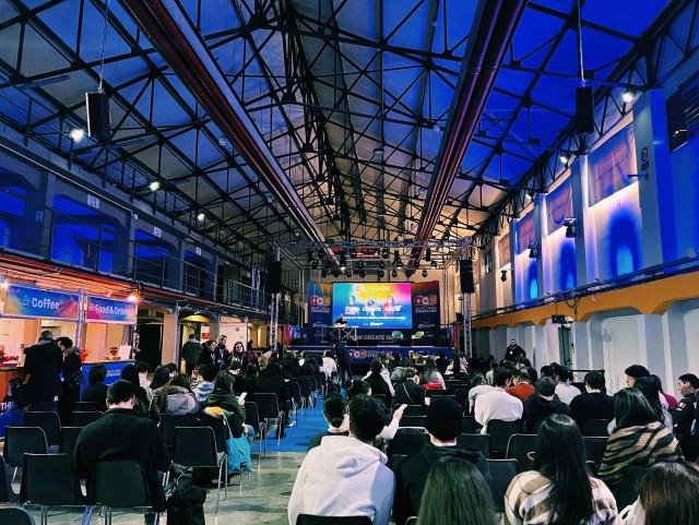 A photo of a conference room with dim blue light in an industrial building - with seats slowly being filled 