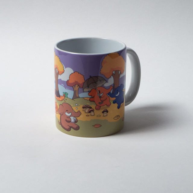 A ceramic mug with a colorful print on it, featuring a blue and a peach colored Mastodon walking under auburn trees, surrounded by mushrooms. One of them is holding an umbrella. Another Mastodon is sitting with a mug of hot beverage.