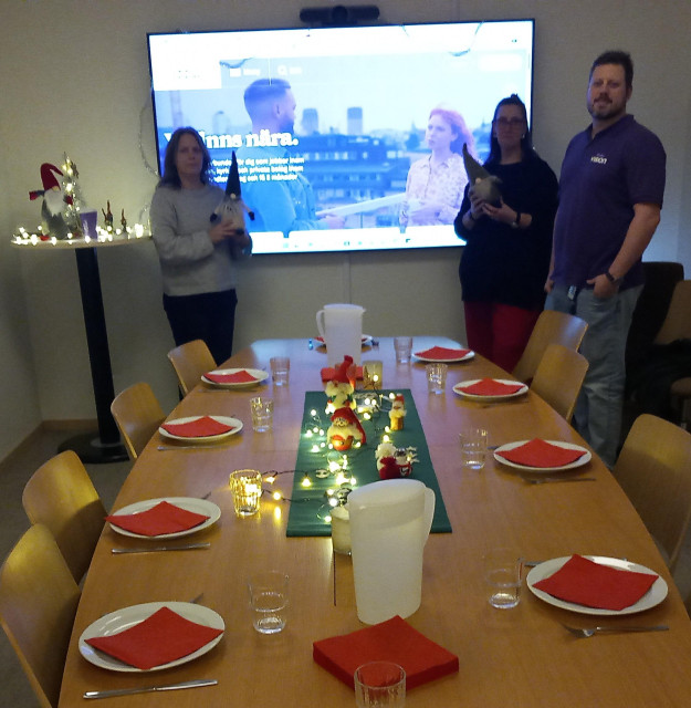 Ett dukat bord med tallrikar med röda servetter. I bortänden står tre personer framför en tv-skärm som visar startsidan av Visions hemsida 