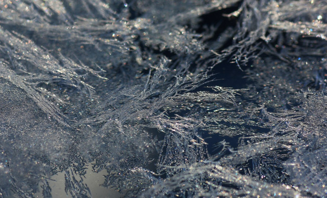 Photograph of frost on several layers of glass, in the form of tangled silver filaments on a blue background.

Photographie de givre sur plusieurs couches de verre, sous forme de filaments enchevêtrés argent sur un fond bleu.