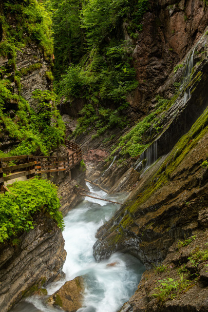Holzstege führen durch eine Klamm mit schroffen, moosbewachsenen Felsen. Der Bach rauscht durch sein Bett
