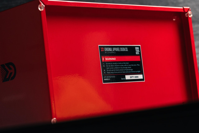 Detail photo of the label on the bottom of the toolbox which was also customized. 

ORIGINAL APPAREL DSGN CO.
MIN
TOOL
BOX.
WARNING!
1.
2.
3.
4.
Do not sit, stand or climb on this item.
Do not allow children to play with or near this item. This
item is not a children's toy storage chest.
Do not use for food contact or food storage.
Keep away from extreme heat and out of direct sunlight.
UPC 931253113123
RMNS5.3
2077-0404
Serial: