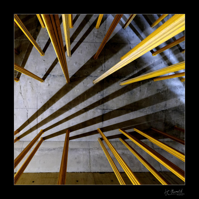 View of a gray concrete surface. Yellow metal supports protrude into the image from all sides and end on the concrete surface. At the bottom left, there is a light source outside the image, causing the supports to cast long dark shadows. The same applies to the upper right corner of the image, where a light source shines into the image from the bottom right. 