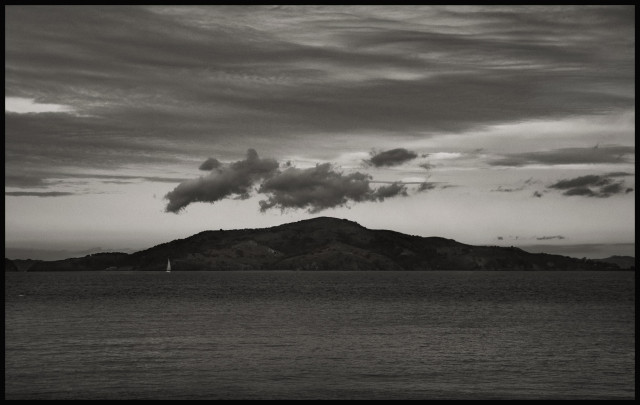 Angel Island, in the San Francisco Bay, under dark, broody skies, surrounded by equally dark bay water.

Above the island's broad hilltop, a trio of dark clouds - puffs of burnt cotton candy - hang in the air. The island is in a bad mood.