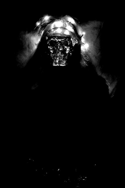 A vertical image with only the head at the top and a few bright reflections from something glittering at the bottom can be seen.
On the head is a halo of light that illuminates the background slightly, as well as the face,  that looks very much like a skull. 
The rest of the image is pitch black.