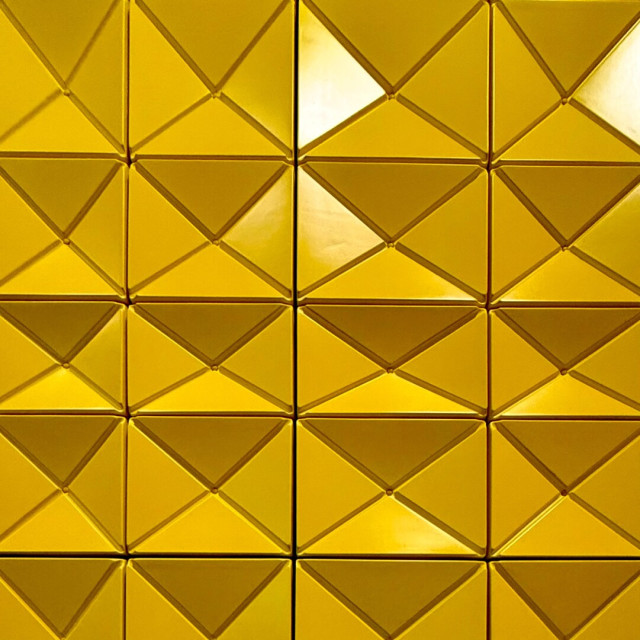 Close up of a yellow tile wall with triangles formed into the shape of rectangles and squares.
