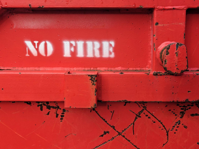 Close up foto of the side of a fire-red skip, with white stencilled words saying “NO FIRE”.