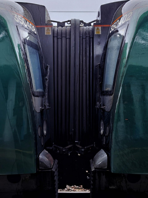 A photo of two green train carriages connected face to face with each other, with a flexible black connector and warning labels between them.