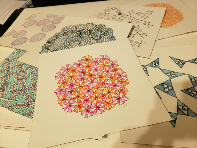 A messy scattering of drawings on watercolor paper on my desk. Some the the patterns are floral.