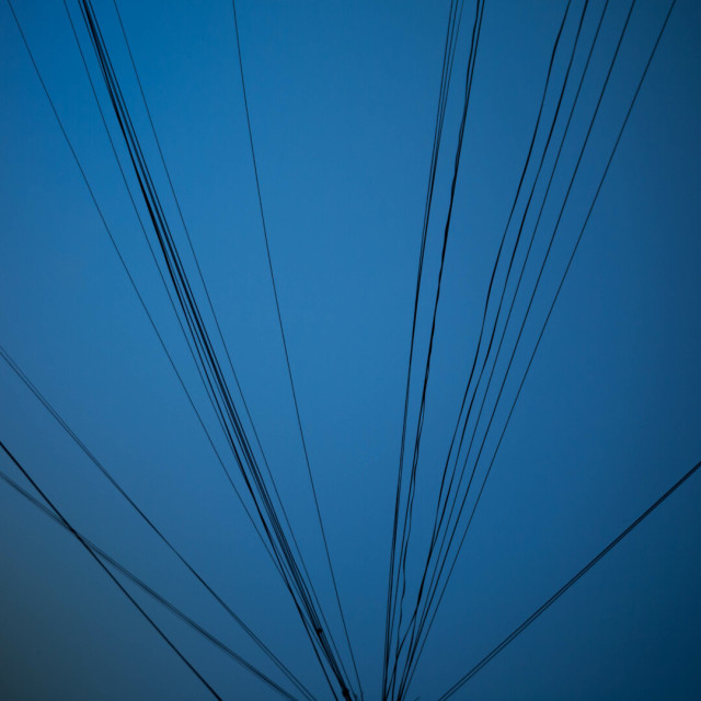 Photo of a faded blue sky with many thin black telephone lines radiating across it from just below the bottom of the from.