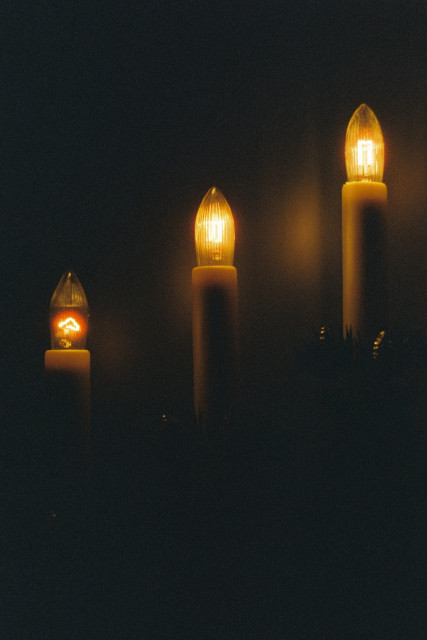Analog close-up photograph of three electric Advent lights. Surrounded by darkness, the tiny incandescent bulbs give off a warm and comforting glow.